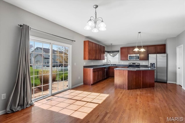 kitchen featuring appliances with stainless steel finishes, a sink, a chandelier, light wood-style flooring, and a center island