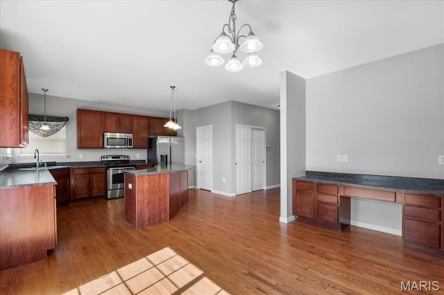 kitchen with stainless steel appliances, a sink, dark wood finished floors, a kitchen island, and hanging light fixtures