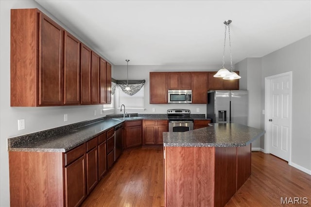 kitchen with stainless steel appliances, a sink, dark countertops, dark wood finished floors, and a kitchen island