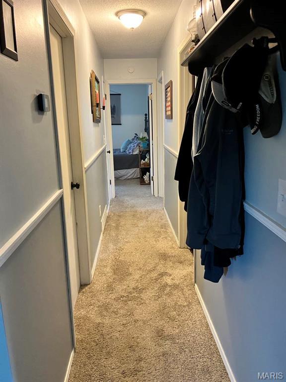 corridor with light carpet and a textured ceiling