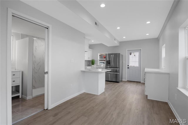 kitchen with stainless steel refrigerator with ice dispenser, light countertops, white cabinets, a peninsula, and light wood-style flooring