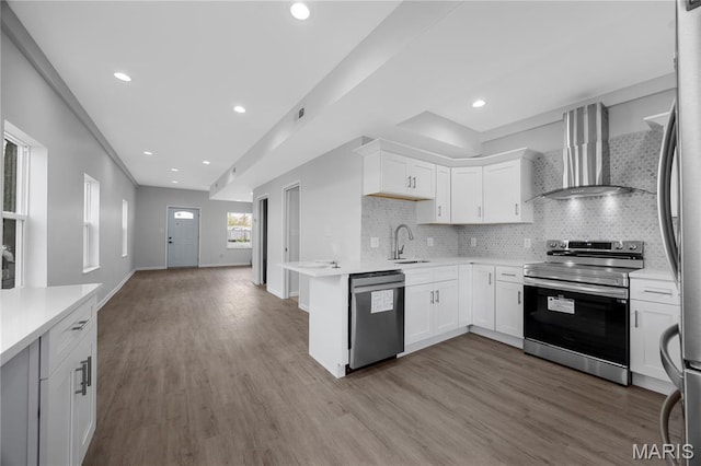 kitchen featuring appliances with stainless steel finishes, wall chimney range hood, a sink, light countertops, and recessed lighting