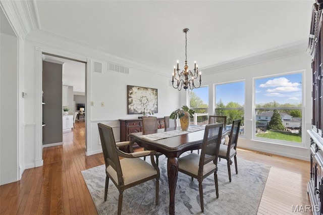 dining area with a chandelier, light wood-style floors, and ornamental molding