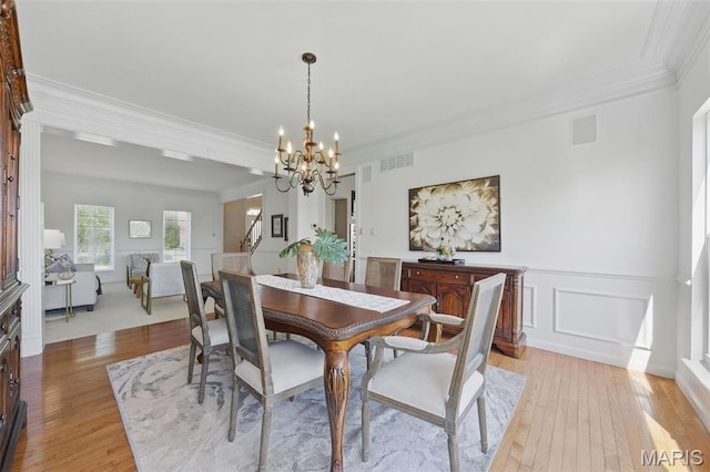 dining room with a chandelier, ornamental molding, light wood-style flooring, wainscoting, and a decorative wall