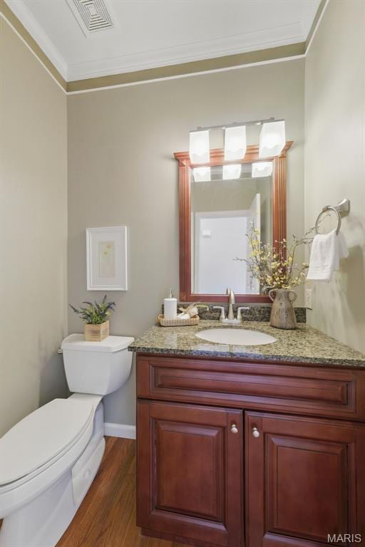 half bathroom with wood finished floors, toilet, ornamental molding, and vanity