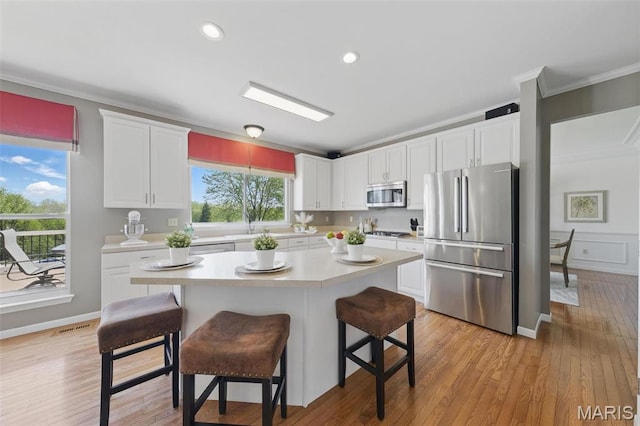 kitchen featuring stainless steel appliances, light countertops, ornamental molding, white cabinets, and a breakfast bar area