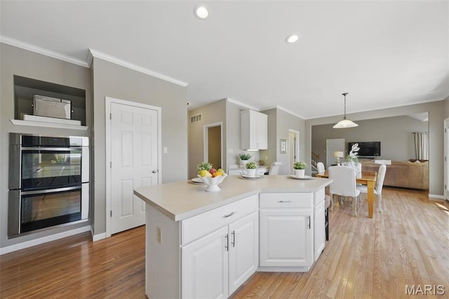 kitchen with stainless steel double oven, white cabinets, light countertops, light wood-style floors, and crown molding
