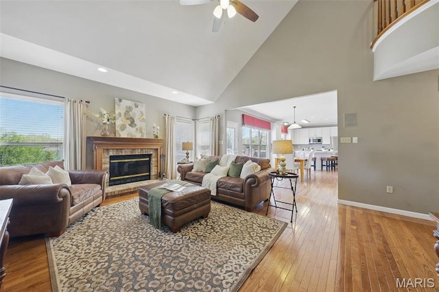 living area with high vaulted ceiling, a ceiling fan, light wood-type flooring, baseboards, and a fireplace
