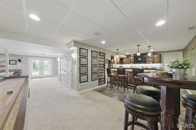 carpeted dining room featuring a drop ceiling, french doors, baseboards, and bar