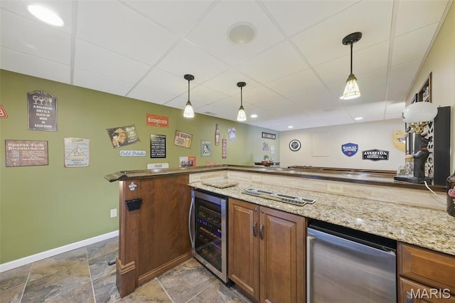 indoor wet bar featuring wine cooler, a paneled ceiling, baseboards, pendant lighting, and stone finish flooring
