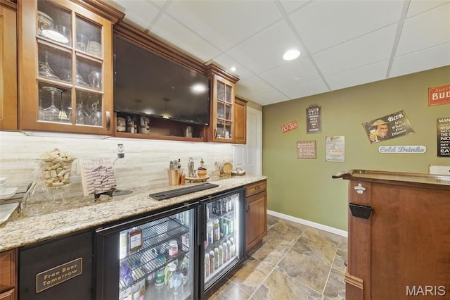 indoor wet bar featuring baseboards, decorative backsplash, stone tile flooring, wine cooler, and a paneled ceiling