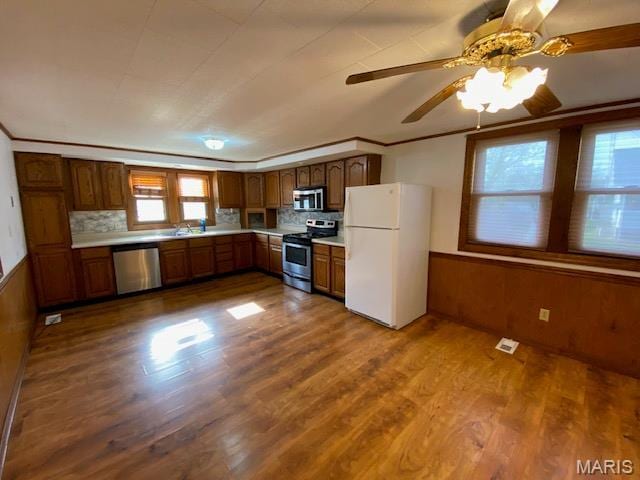 kitchen with stainless steel appliances, plenty of natural light, light countertops, dark wood finished floors, and wainscoting