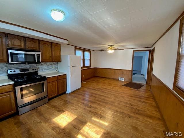 kitchen featuring appliances with stainless steel finishes, a wainscoted wall, wood finished floors, ceiling fan, and light countertops
