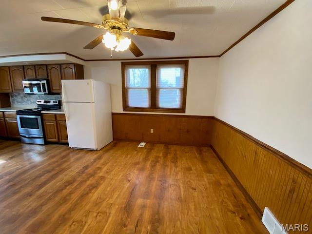 kitchen featuring stainless steel appliances, wainscoting, wood finished floors, light countertops, and wood walls