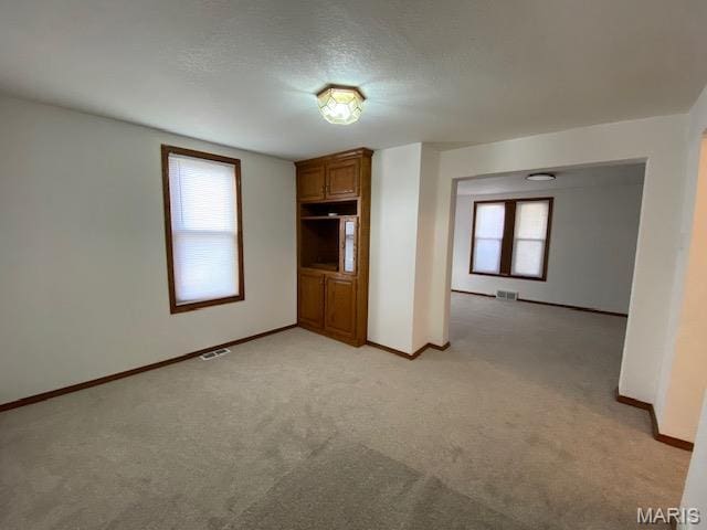 unfurnished living room featuring light colored carpet and baseboards