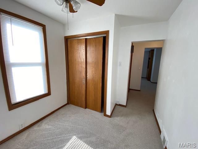 unfurnished bedroom with light colored carpet, a closet, baseboards, and ceiling fan