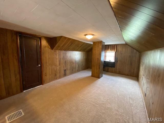 additional living space featuring wooden walls, light carpet, and lofted ceiling