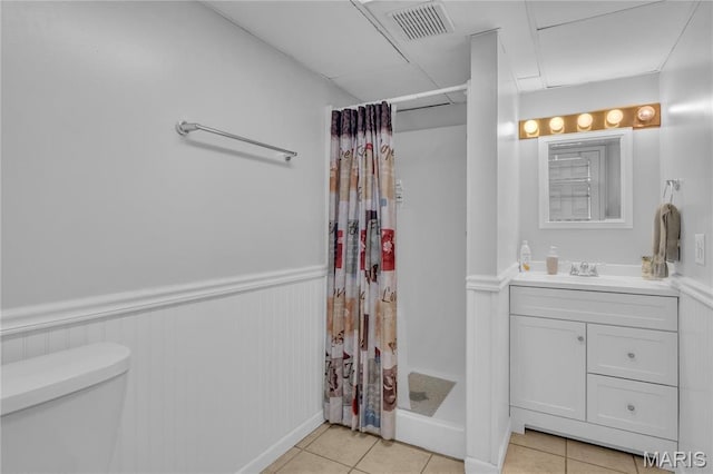 bathroom with a stall shower, toilet, a wainscoted wall, tile patterned floors, and vanity