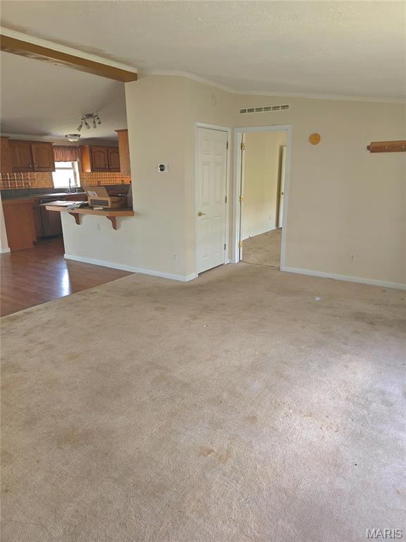 unfurnished living room with carpet flooring, baseboards, lofted ceiling, crown molding, and wood finished floors