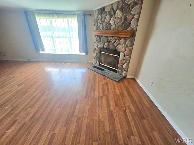 unfurnished living room featuring baseboards, a stone fireplace, and wood finished floors