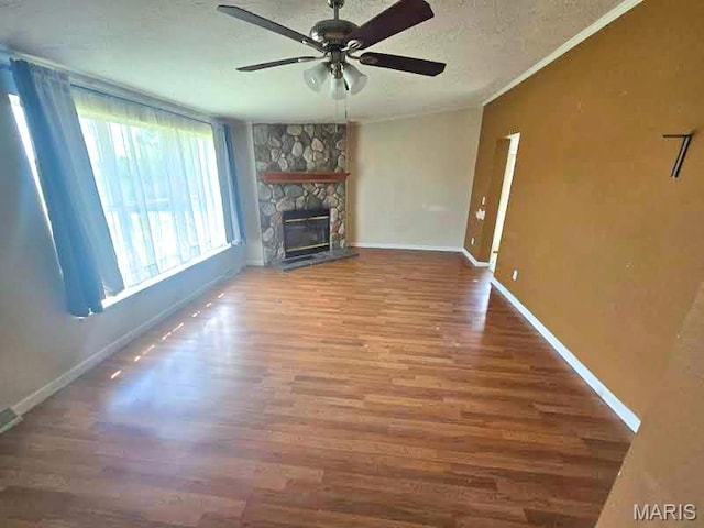 unfurnished living room featuring a ceiling fan, wood finished floors, a stone fireplace, baseboards, and ornamental molding