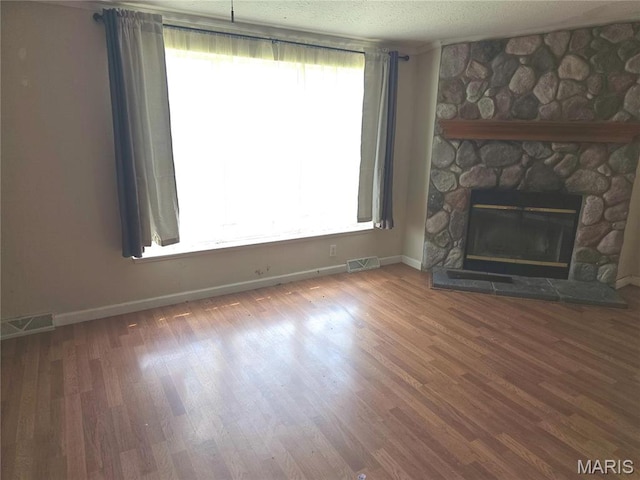 unfurnished living room with baseboards, wood finished floors, a stone fireplace, and a textured ceiling