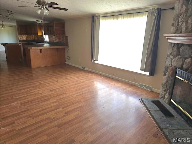 unfurnished living room featuring ceiling fan, a fireplace, healthy amount of natural light, a sink, and a textured ceiling