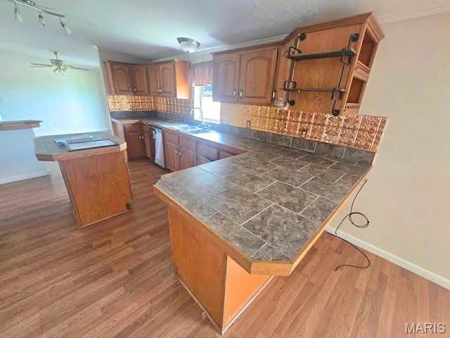 kitchen featuring dishwasher, a sink, brown cabinetry, and decorative backsplash
