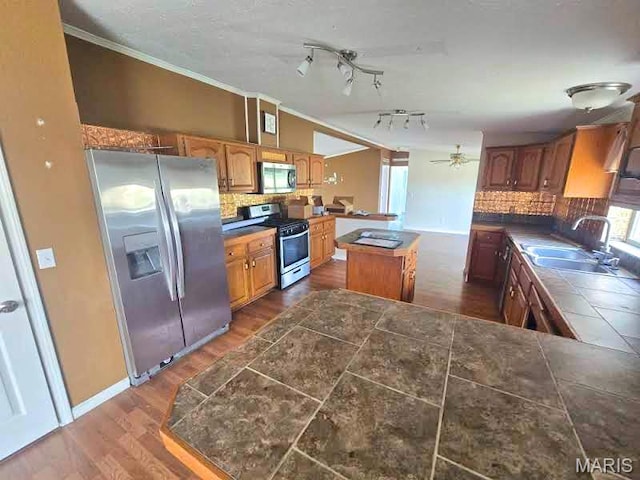 kitchen with stainless steel appliances, a sink, backsplash, a kitchen island, and dark wood-type flooring