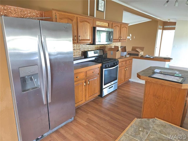 kitchen featuring appliances with stainless steel finishes, wood finished floors, crown molding, tasteful backsplash, and tile countertops
