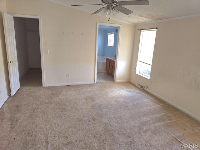 unfurnished bedroom featuring a walk in closet, light carpet, baseboards, crown molding, and ensuite bath