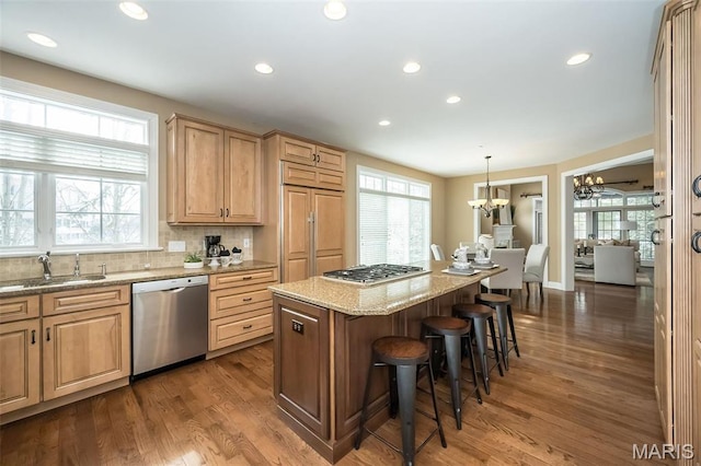 kitchen with stainless steel appliances, a kitchen bar, a chandelier, light stone counters, and a sink