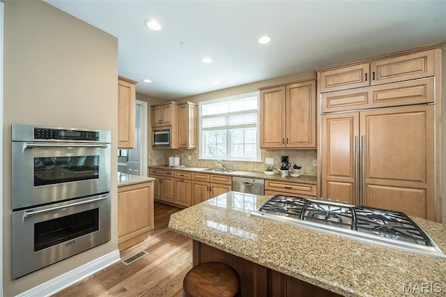 kitchen with appliances with stainless steel finishes, light wood finished floors, a sink, tasteful backsplash, and light brown cabinets