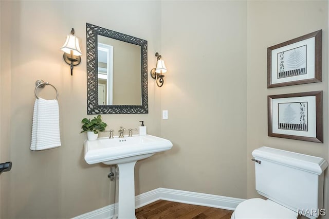 half bath featuring baseboards, wood finished floors, and toilet