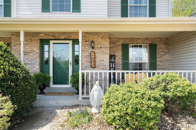doorway to property featuring covered porch and brick siding