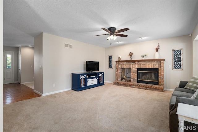 living area with carpet floors, a ceiling fan, a fireplace, baseboards, and a textured ceiling