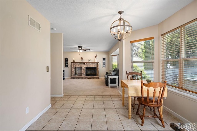 dining area with light colored carpet, a chandelier, light tile patterned flooring, a brick fireplace, and ceiling fan