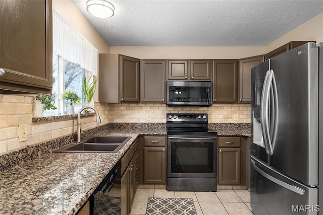kitchen featuring appliances with stainless steel finishes, a sink, dark stone countertops, light tile patterned floors, and tasteful backsplash
