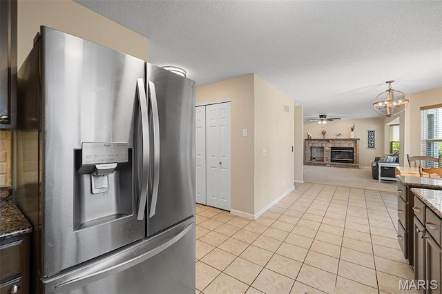 kitchen with stainless steel fridge, light tile patterned floors, a chandelier, dark stone counters, and a fireplace