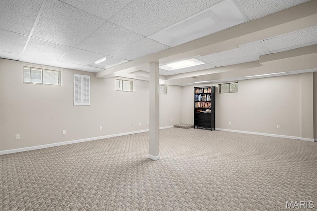 basement featuring a paneled ceiling, carpet flooring, baseboards, and plenty of natural light