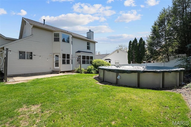 back of house with a chimney, entry steps, a lawn, a covered pool, and a patio