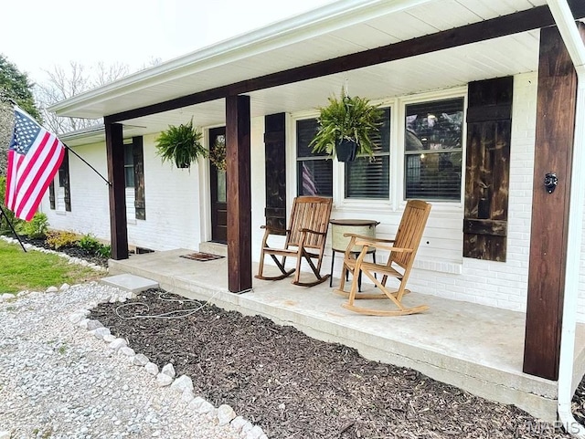 doorway to property featuring covered porch and brick siding