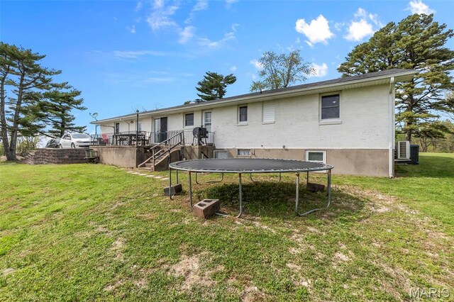 back of property featuring a trampoline, stairway, a lawn, and brick siding
