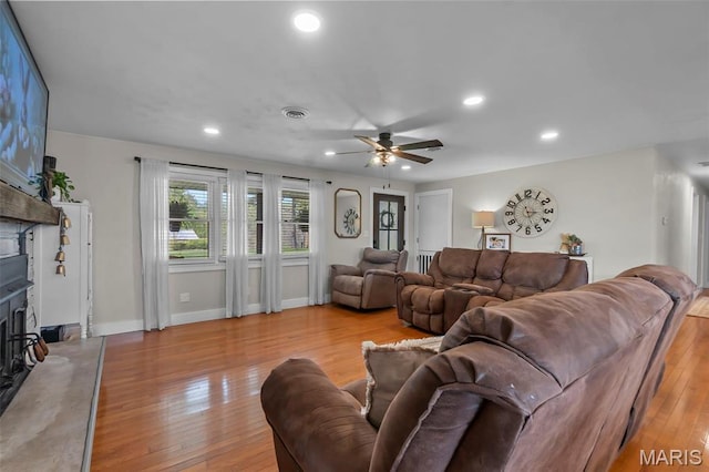 living room with hardwood / wood-style floors, a fireplace with raised hearth, a ceiling fan, recessed lighting, and baseboards
