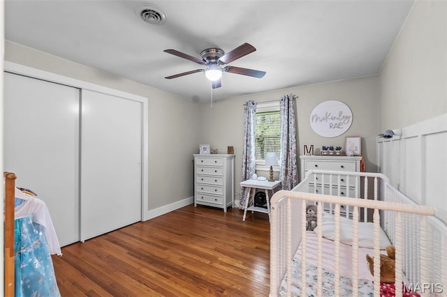 bedroom with wood finished floors, a closet, a nursery area, and ceiling fan