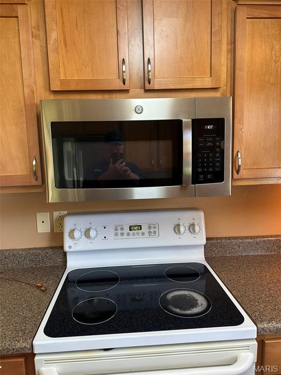 142 Oregon Ln, Kimberling City, MO 65686 - kitchen view of stainless steel microwave, electric range, dark countertops, and brown cabinetry