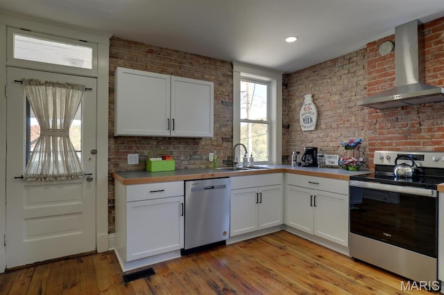 kitchen with stainless steel appliances, wall chimney exhaust hood, a sink, white cabinetry, and light wood-style flooring
