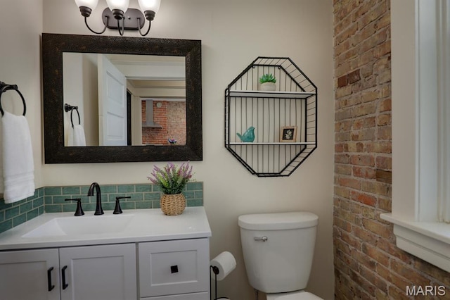 bathroom featuring toilet, vanity, a chandelier, and brick wall