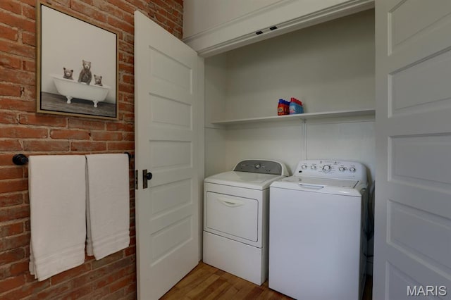 clothes washing area with washer and dryer, wood finished floors, and brick wall