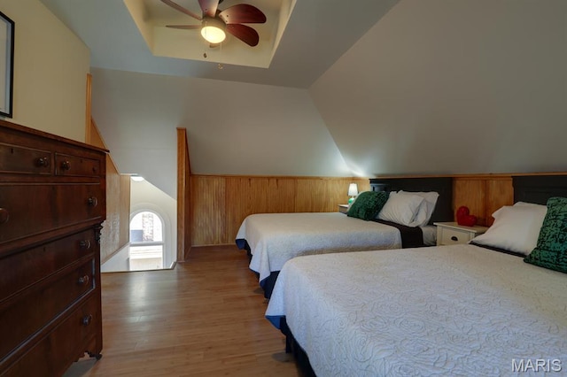 bedroom featuring light wood-type flooring, vaulted ceiling, a ceiling fan, wooden walls, and a wainscoted wall